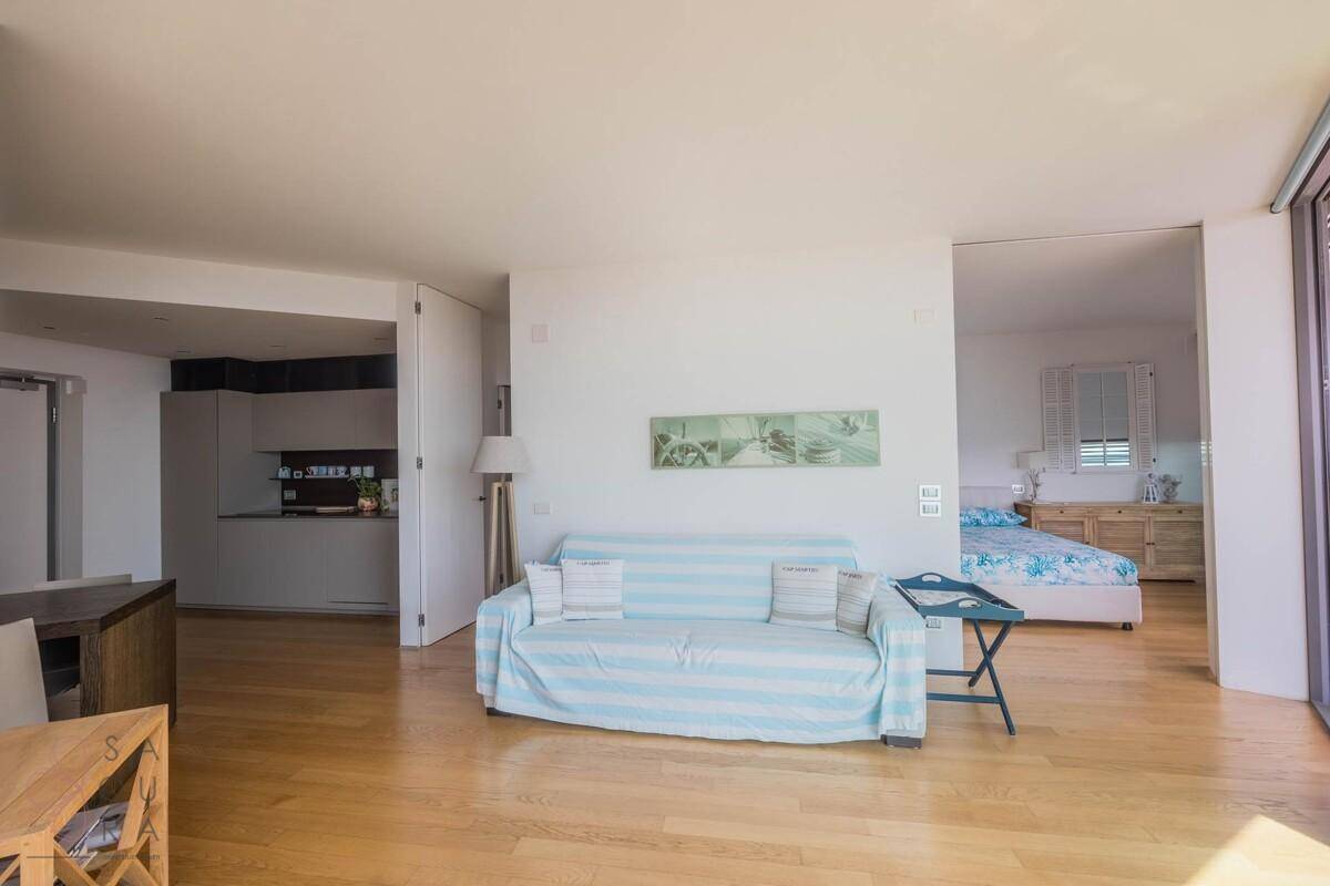 Offener Wohnbereich mit gestreiftem Sofa, Holzboden und Übergang zur Küche und zum Schlafzimmer.