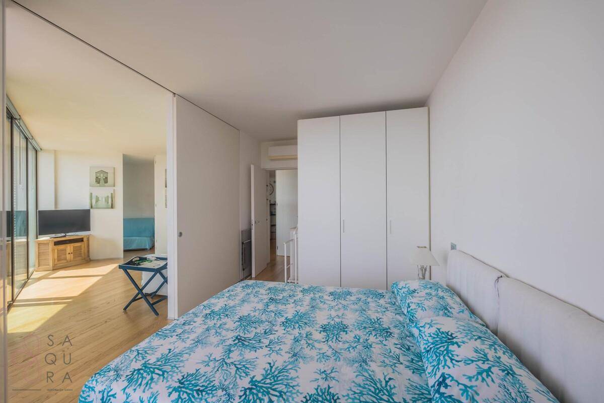 Schlafzimmer mit Doppelbett und weißen Einbauschränken, offen zum angrenzenden Wohnbereich.