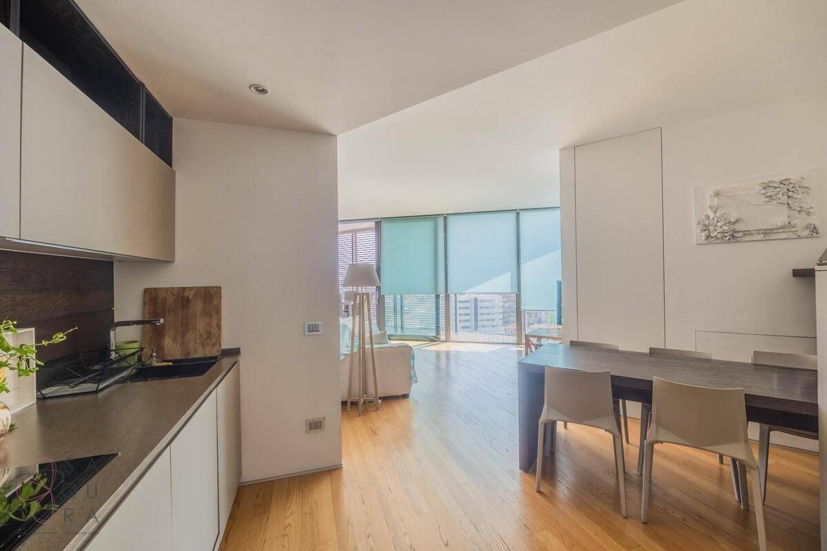 Moderne Küche mit Essbereich, Holzboden und Blick in den hellen Wohnbereich mit großen Fenstern.