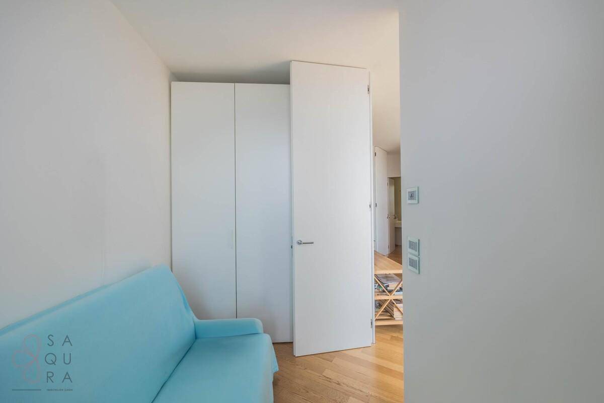 Gemütlicher Raum mit blauem Schlafsofa und praktischen weißen Einbauschränken.