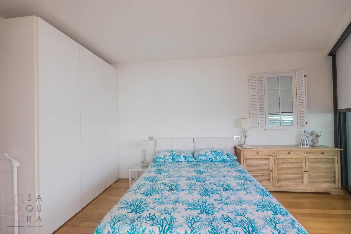 Helles Schlafzimmer mit Doppelbett, weißen Einbauschränken und dekorativem Fenster-Spiegel.