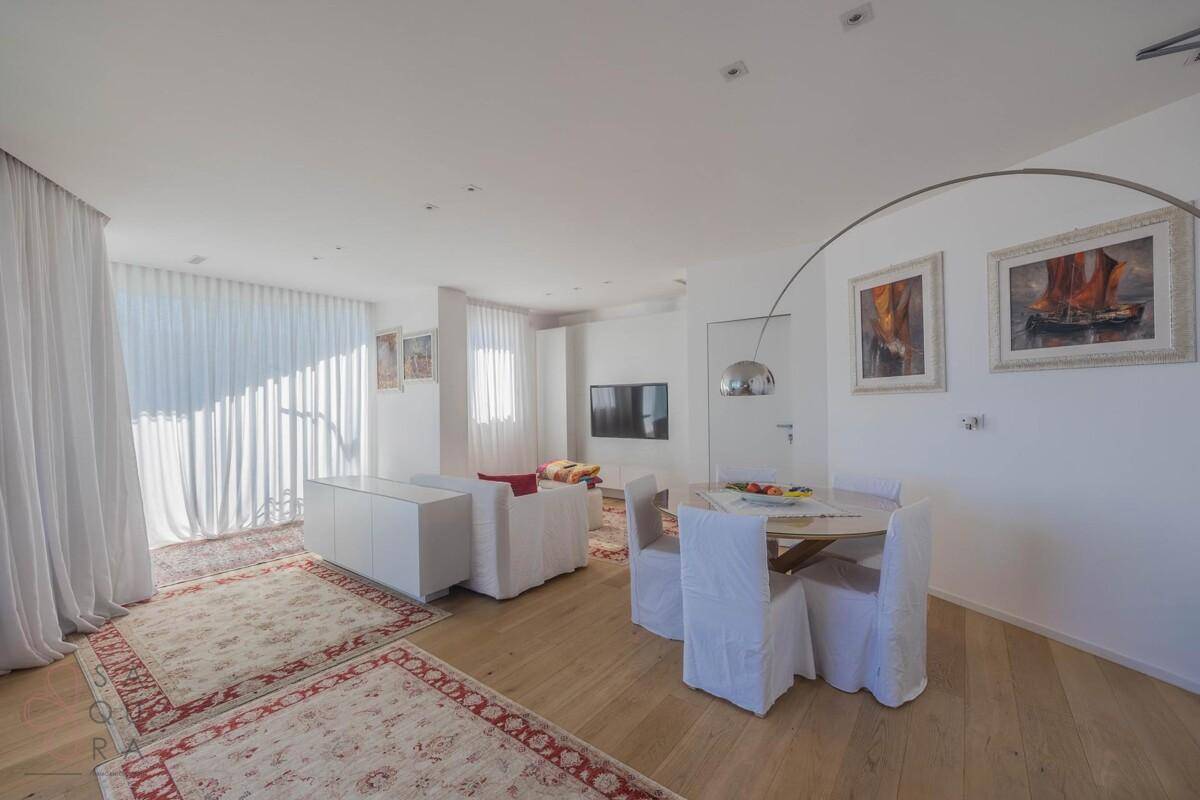 Helles Wohn-Esszimmer mit Holzboden, weißen Möbeln und dekorativen Teppichen.