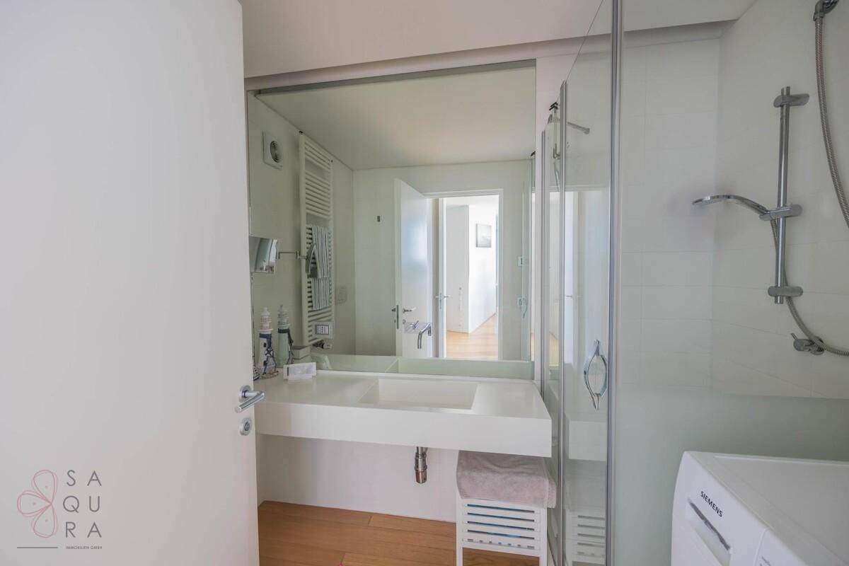 Modernes Badezimmer mit Dusche, Einzelwaschbecken, großem Spiegel und beheiztem Handtuchhalter.