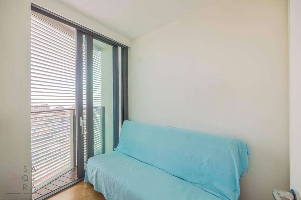 Kleiner Raum mit blauem Schlafsofa und großen Schiebetüren zum Balkon.