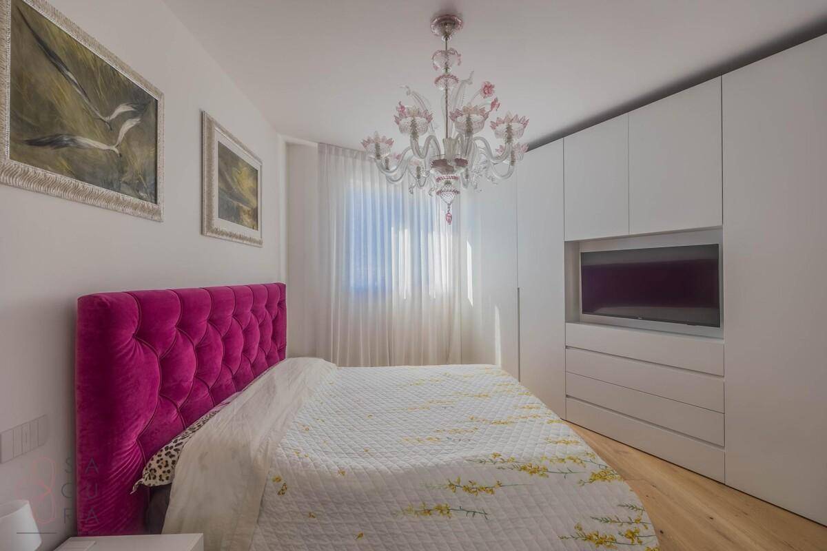 Gemütliches Schlafzimmer mit pinkem Kopfteil, Holzboden und integriertem TV in den Schränken.
