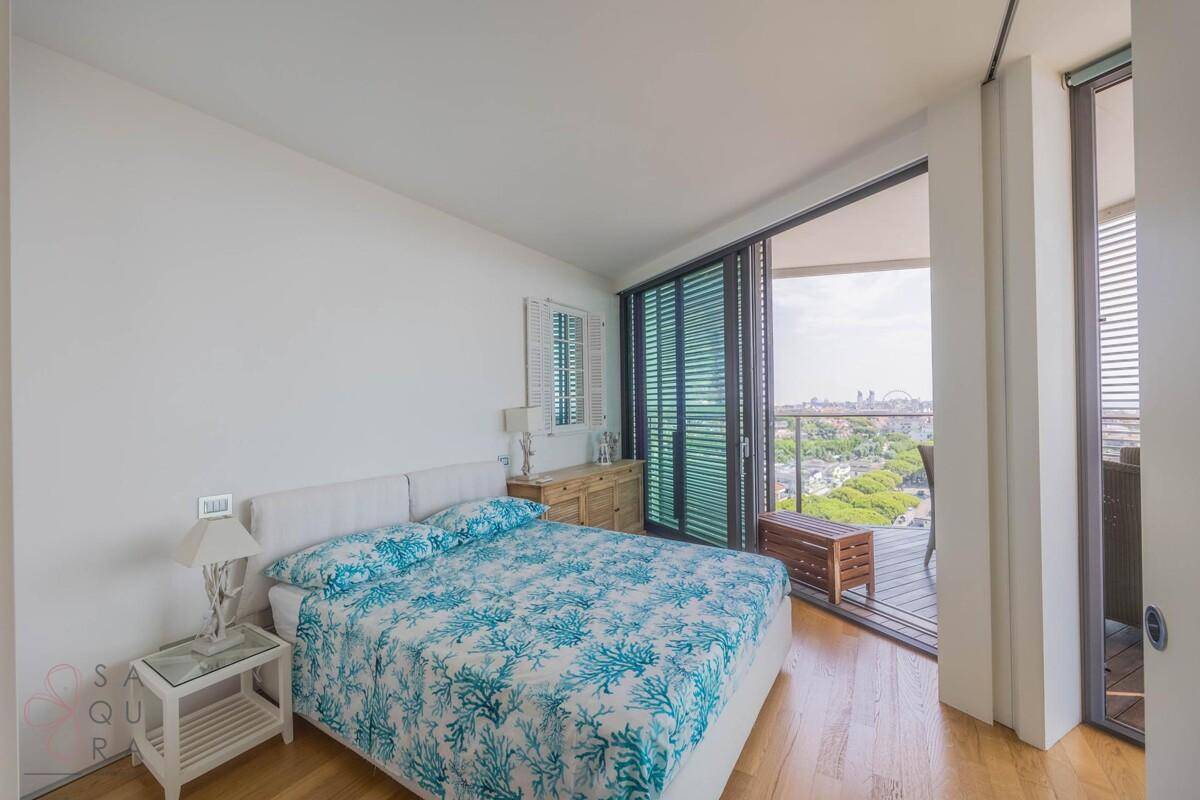 Schlafzimmer mit Doppelbett, Holzboden und Zugang zu einem Balkon mit weitem Stadtblick.