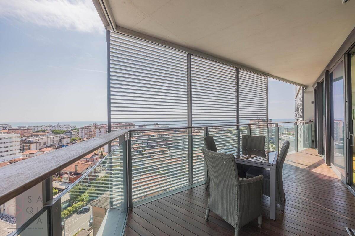 Großer Balkon mit modernen Sitzmöbeln, Holzdeck und weitem Blick über die Stadt und das Meer.