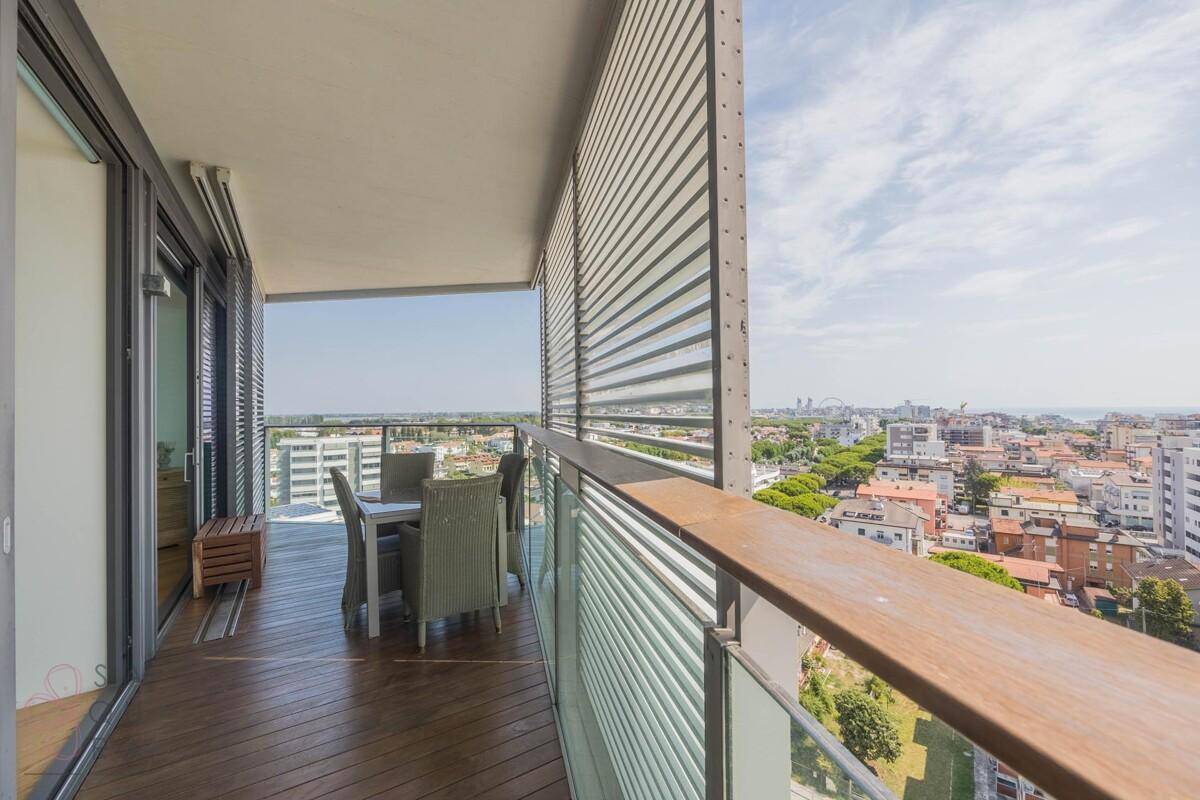 Geräumiger Balkon mit Holzdeck, Sitzgelegenheiten und Panoramablick über die Stadt zum Meer.