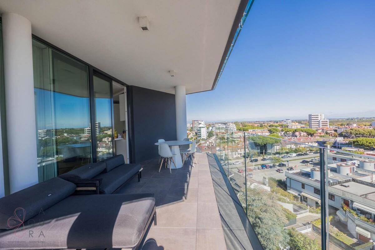 Moderner Balkon mit Glasgeländer, Lounge-Möbeln und weitem Blick über die Stadt.