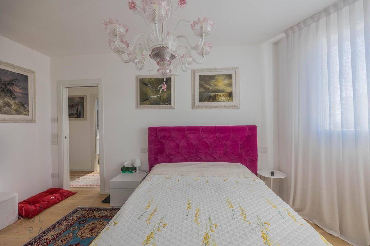 Schlafzimmer mit Holzboden, pinkem Bett und Zugang zu einem weiteren Raum.