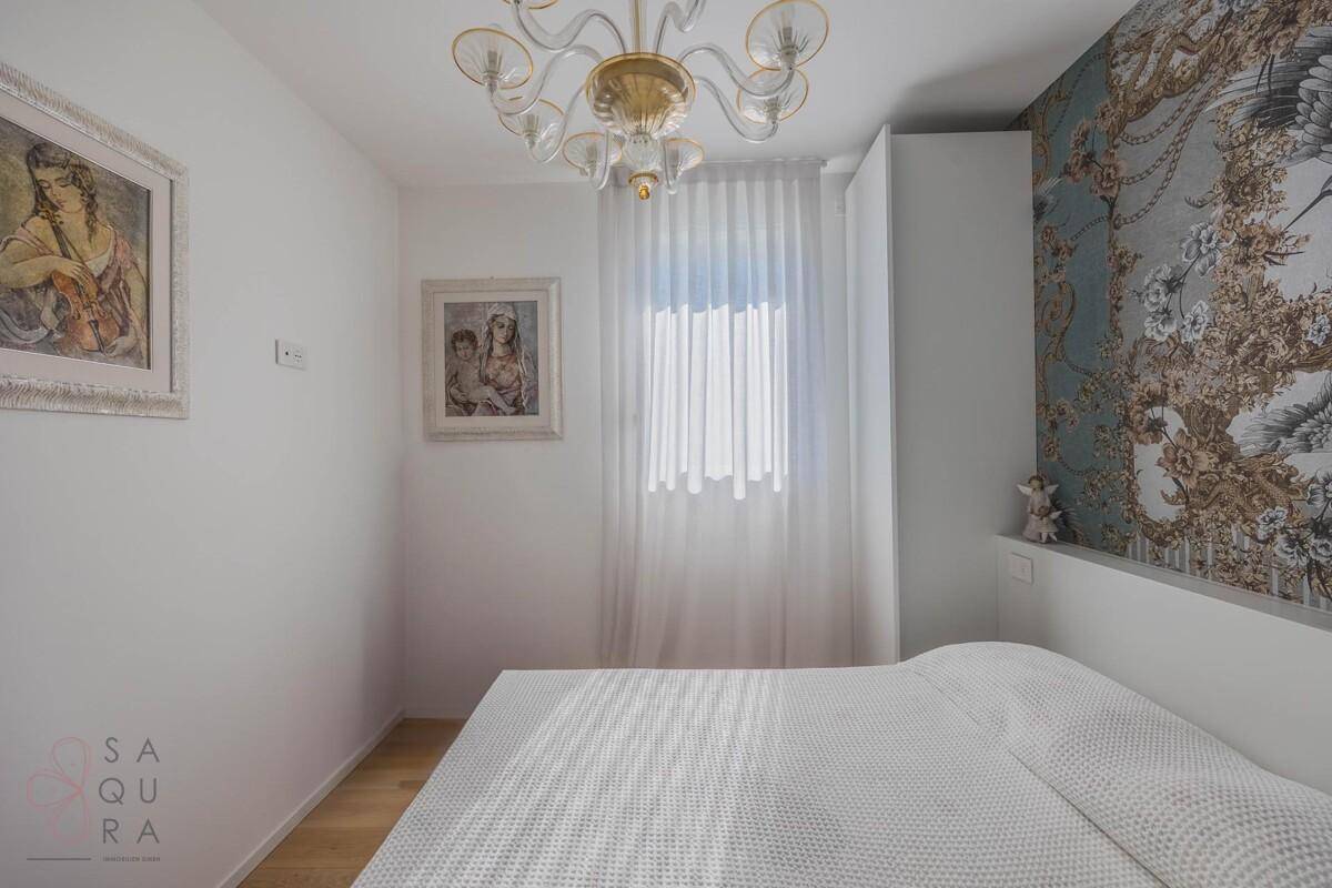 Helles Schlafzimmer mit Holzboden, Fenster und einer auffälligen Wandtapete.