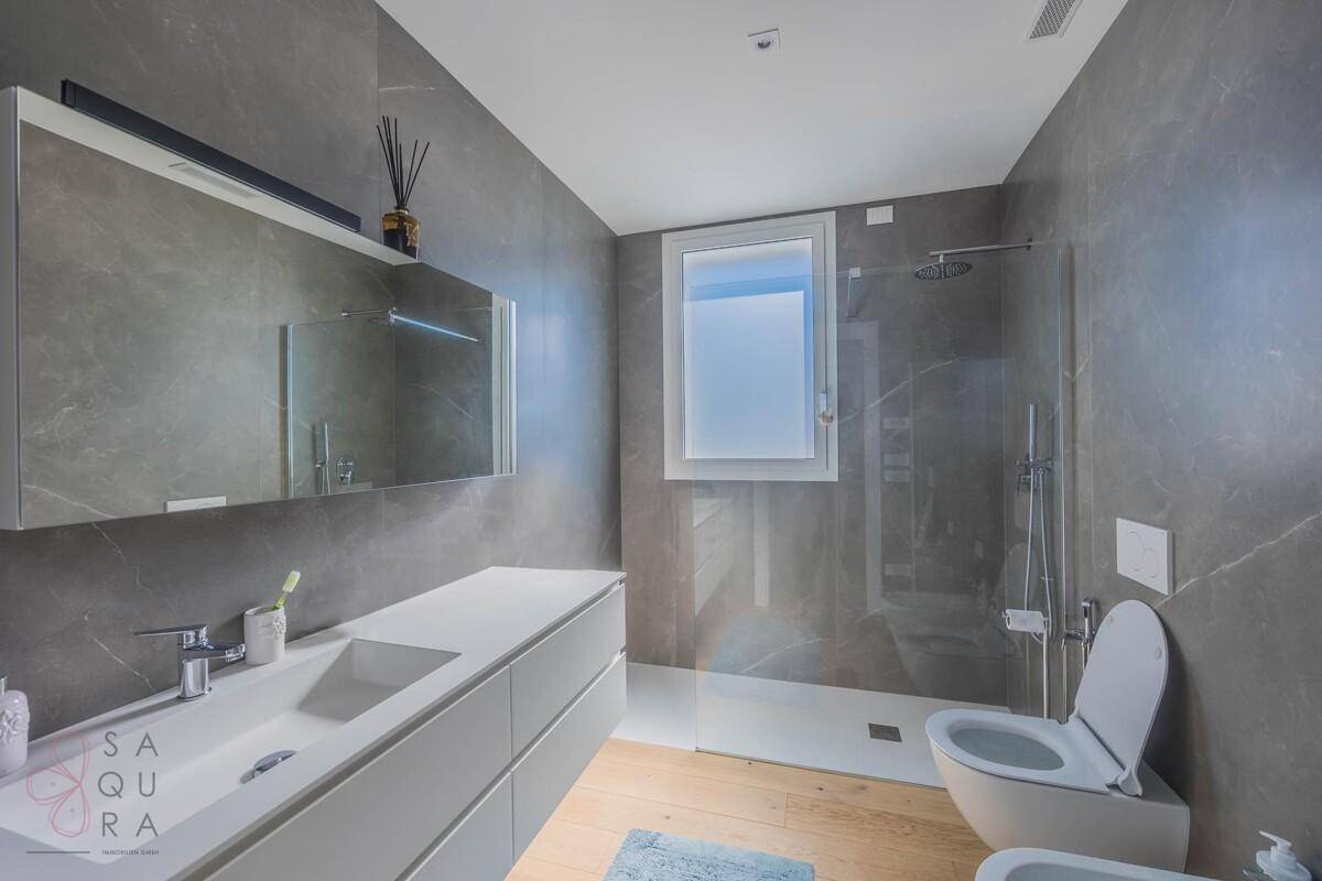 Modernes Badezimmer mit grauen Fliesen, Doppelwaschbecken und begehbarer Dusche.
