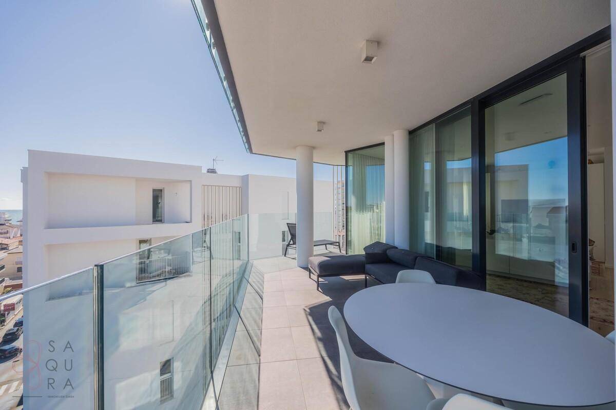 Geräumiger Balkon mit Glasgeländer, Sitzgelegenheiten und weitem Stadtblick.