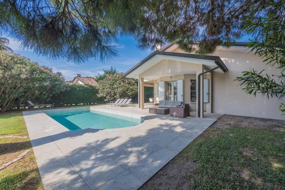 Seitliche Ansicht des Hauses mit Pool und gepflasterter Terrasse, umgeben von grüner Vegetation und Bäumen.