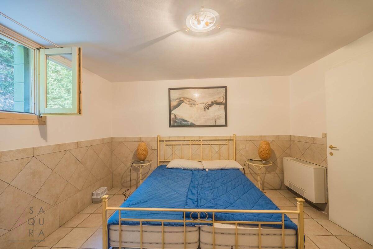 Schlafzimmer im Untergeschoss mit Doppelbett, Fliesenboden und einem Kunstwerk an der Wand.
