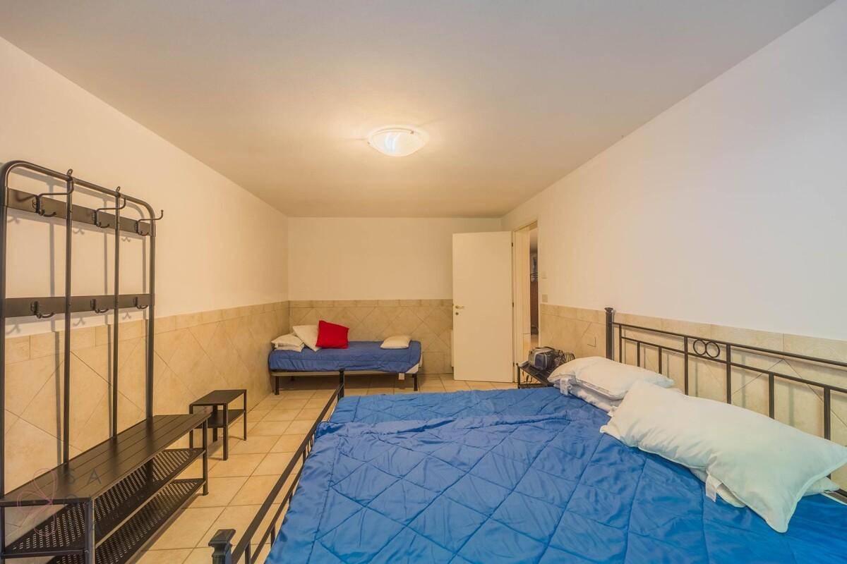 Schlafzimmer im Untergeschoss mit zwei Betten, Fliesenboden und schlichter, funktionaler Einrichtung.