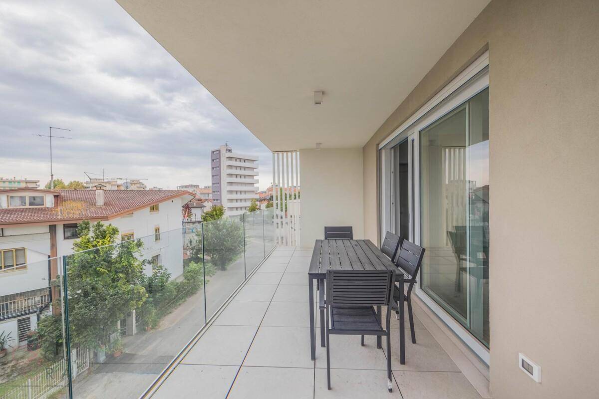 Langer Balkon mit modernem Glasgeländer und Essbereich im Freien, mit Stadtblick.