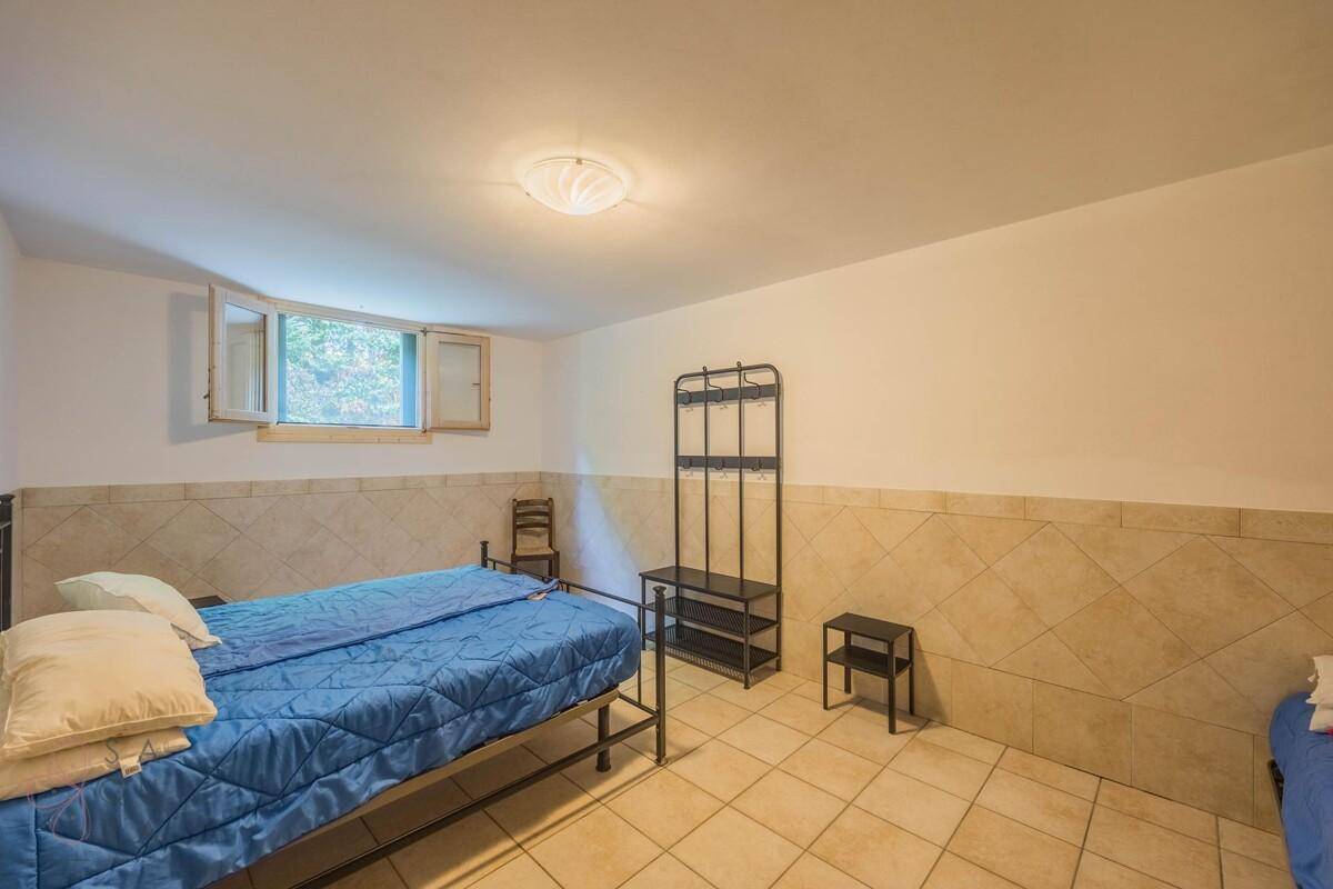 Einfaches Schlafzimmer im Kellergeschoss mit Fliesenboden und einem kleinen Fenster für Tageslicht.