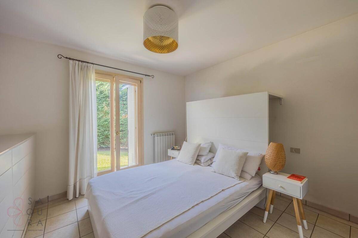 Helles Schlafzimmer mit weißem Bett, Fliesenboden und direktem Zugang zum Garten.