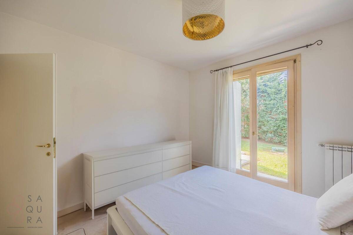 Geräumiges Schlafzimmer mit weißer Kommode, Fliesenboden und Blick ins Grüne.