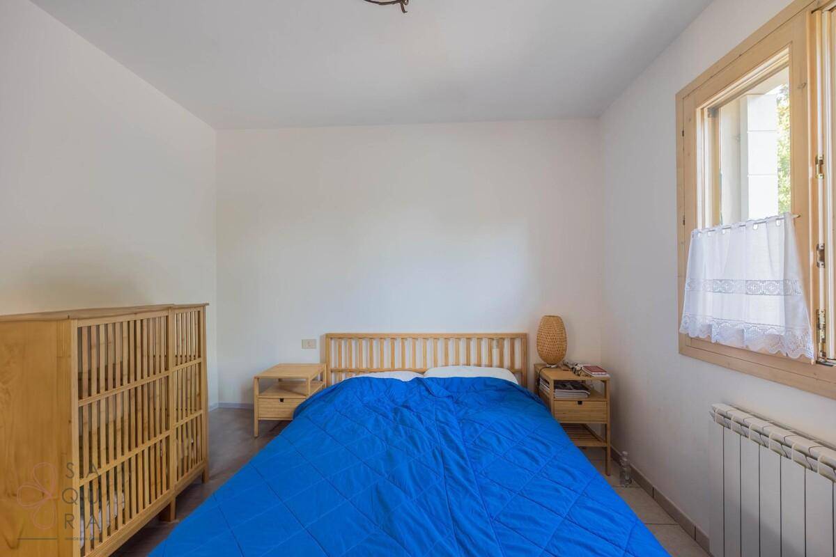 Schlafzimmer mit Holzbett und Kommode, Fliesenboden und einem Fenster, das viel Licht hereinlässt.