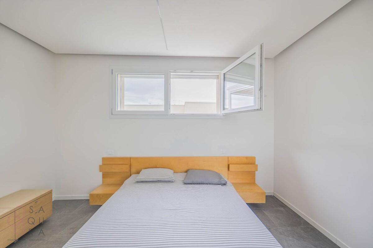Schlafzimmer mit modernem Holzbett, Nachttisch und großen Fenstern für viel Tageslicht.