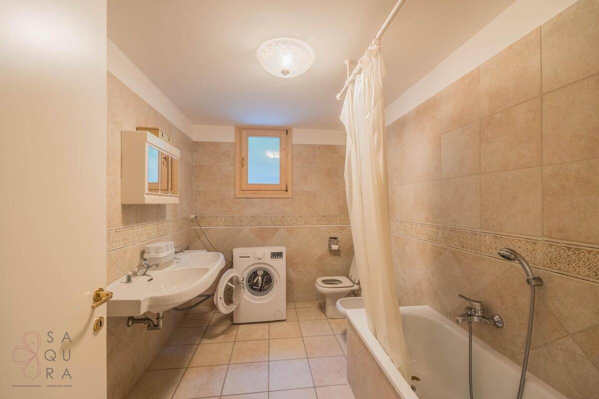 Funktionales Badezimmer mit Badewanne, Waschmaschine und beigefarbenen Fliesen.