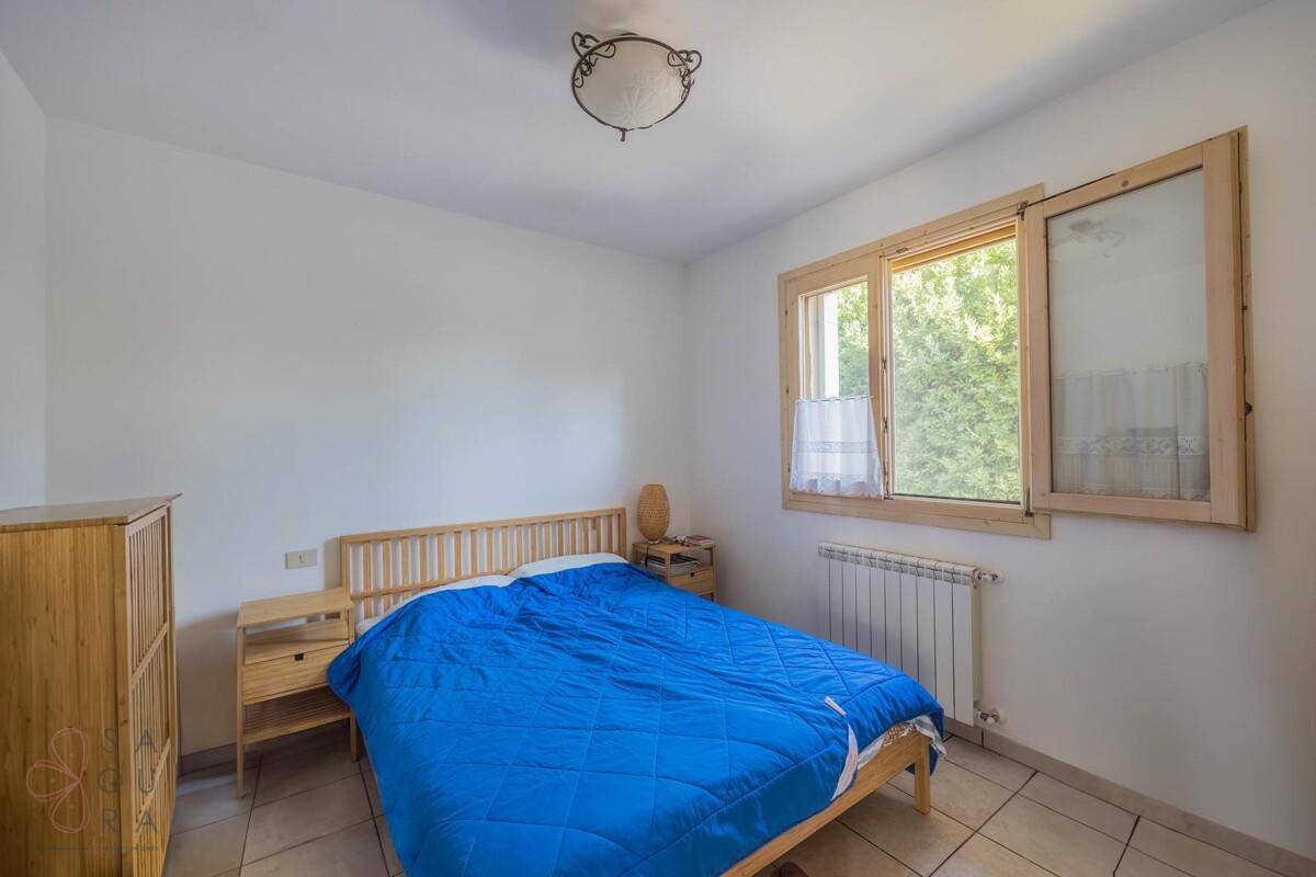 Helles Schlafzimmer mit Holzmöbeln, Fliesenboden und einem Fenster mit Blick ins Grüne.