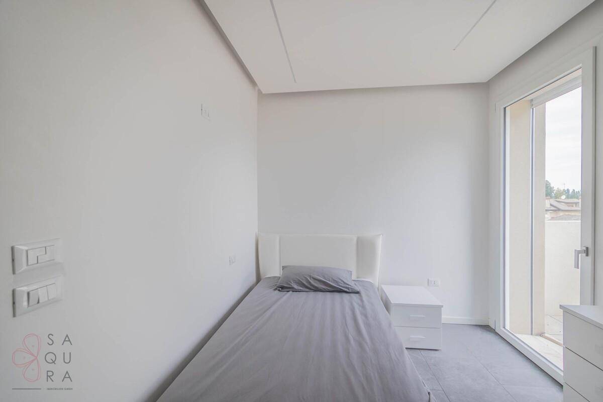 Kleines Schlafzimmer mit Einzelbett, weißem Mobiliar und direktem Balkonzugang.