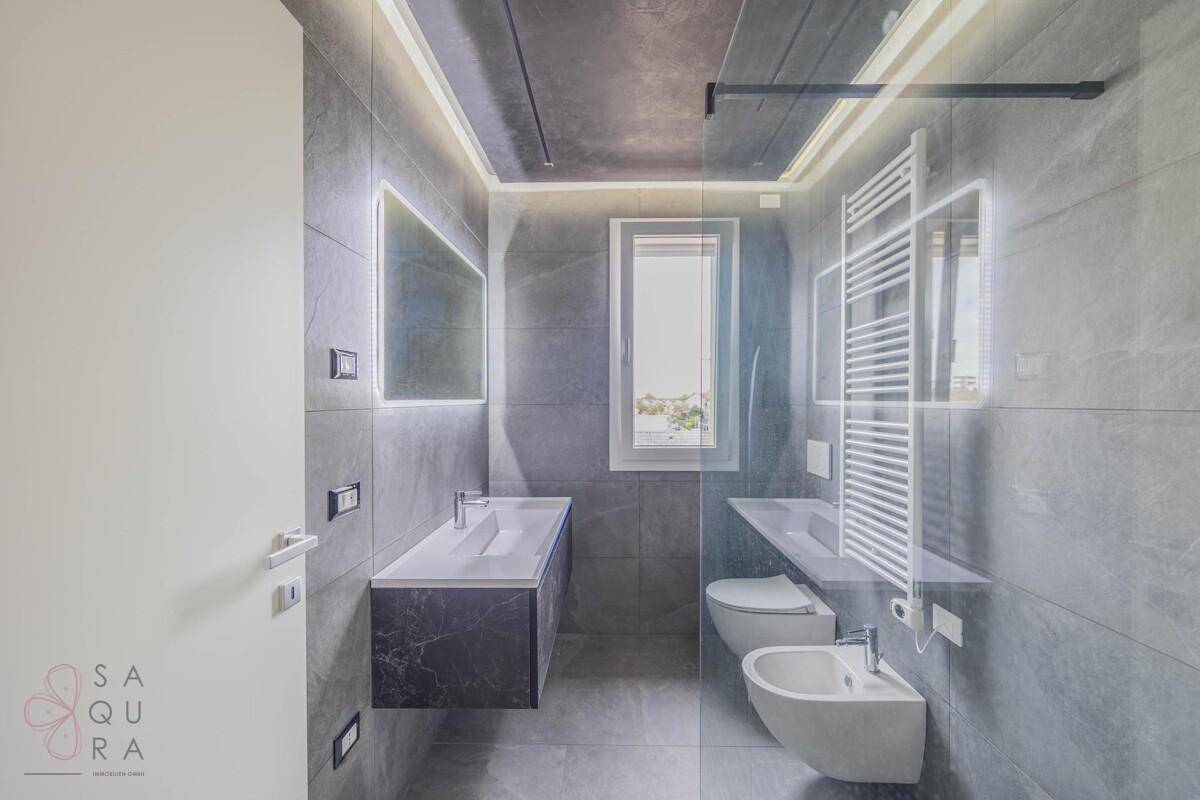 Modernes Badezimmer mit grauen Fliesen, Doppelwaschbecken, Bidet und begehbarer Dusche.