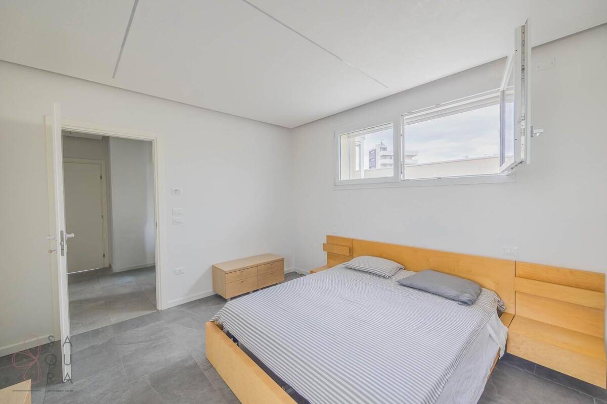 Helles Schlafzimmer mit Holzbett und Zugang zum Flur, ausgestattet mit Fliesenboden.
