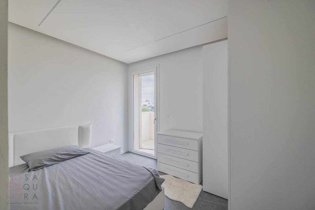 Schlafzimmer mit weißer Kommode und Zugang zu einem kleinen Balkon, hell und modern.