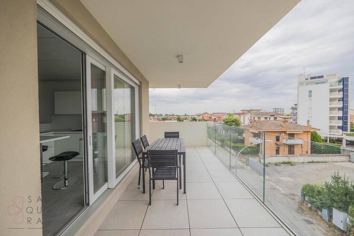 Geräumiger Balkon mit Esstisch und Stühlen, Glasgeländer und Blick auf die Umgebung.