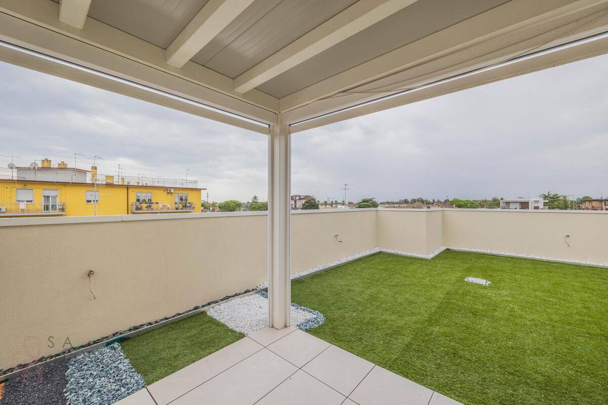 Eckansicht der Dachterrasse mit Kunstrasen, Zierkies und überdachtem Sitzbereich.