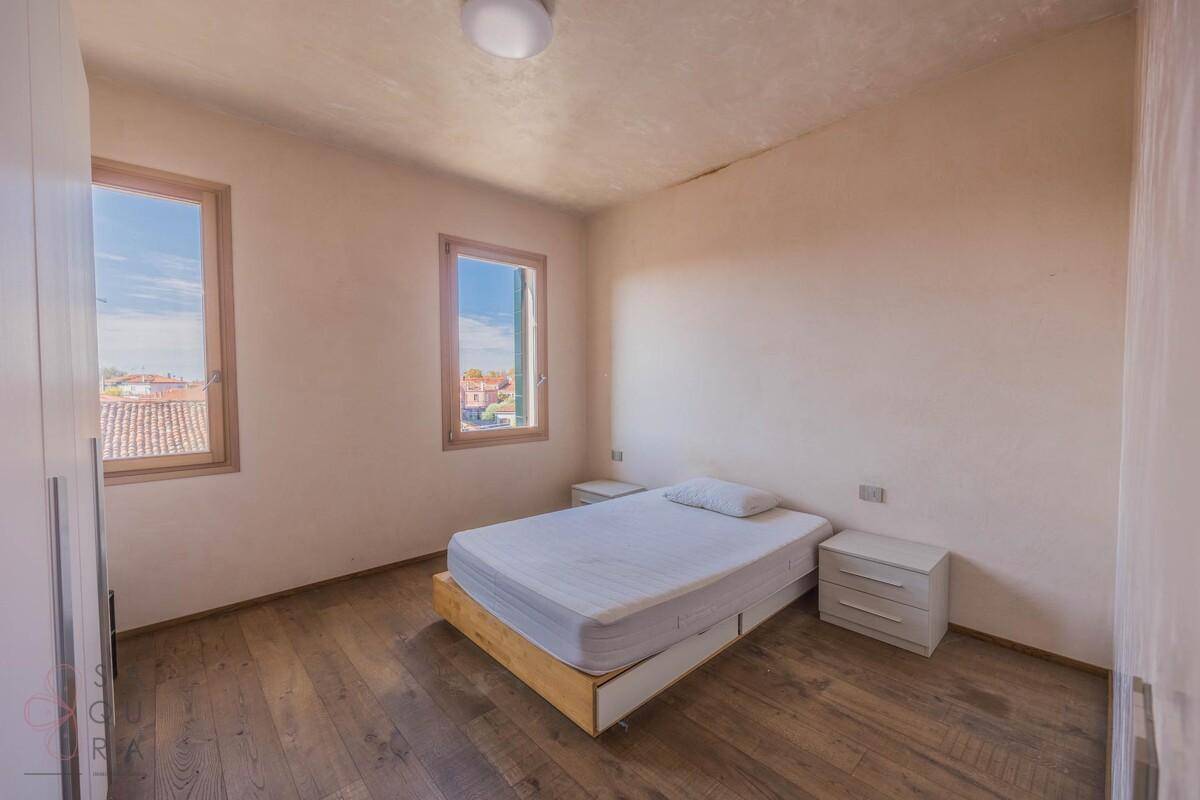 Helles Schlafzimmer mit Holzboden, einem Einzelbett und Fenstern mit Blick über die Dächer.