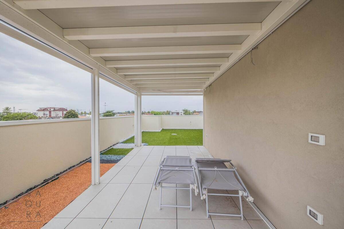 Überdachter Bereich der Dachterrasse mit Liegestühlen und Blick auf die Grünfläche.
