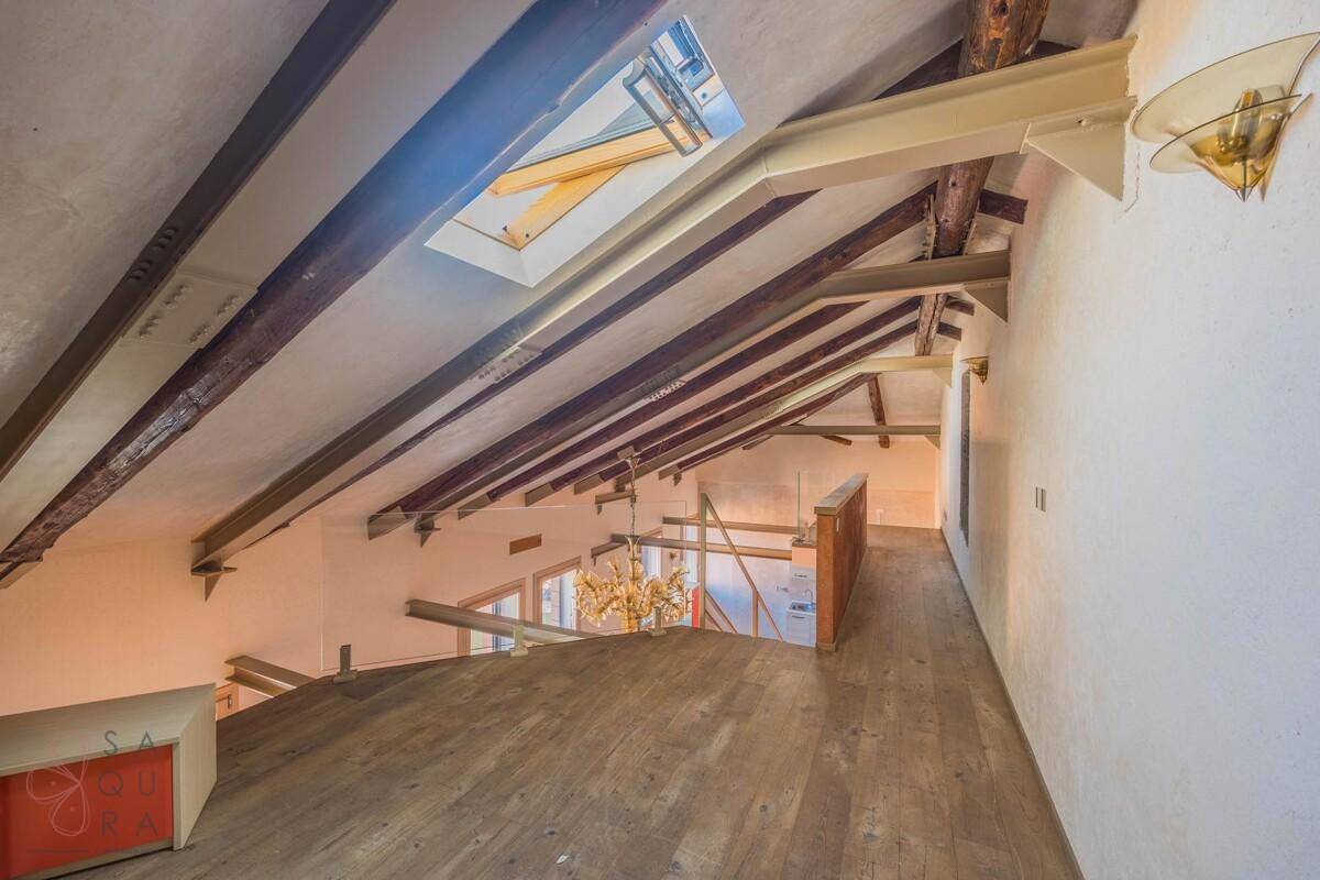 Dachgeschoss mit sichtbaren Holzbalken, Dachfenster und Blick hinunter in den offenen Wohnbereich.