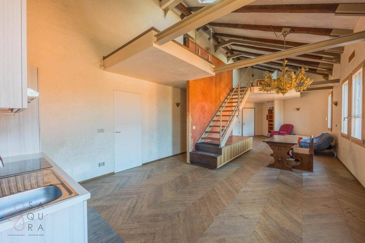 Offener Wohnbereich mit integrierter Küchenzeile, Fischgrätparkett und einer Treppe zum Dachgeschoss.