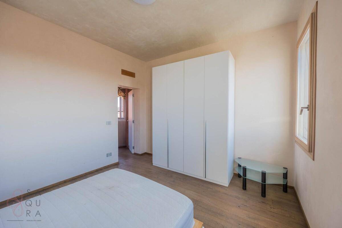 Schlafzimmer mit Holzboden, weißem Kleiderschrank und einem Durchgang zu einem weiteren Bereich.