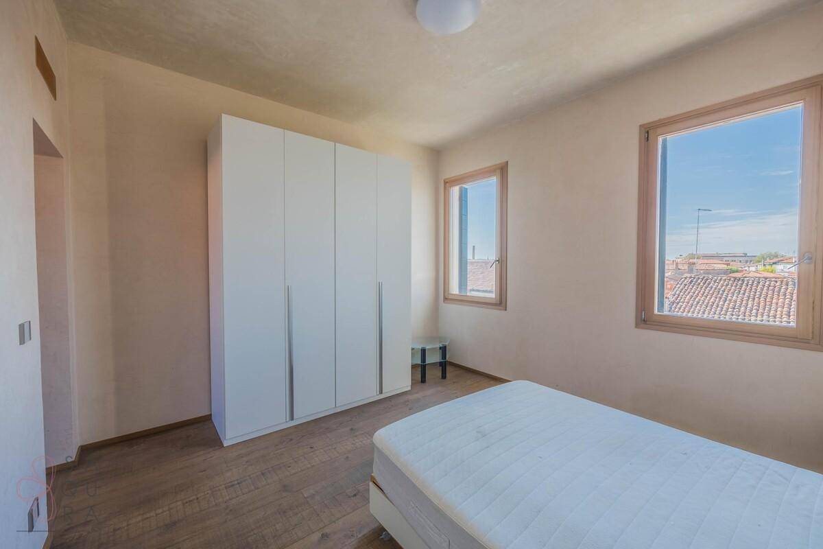 Schlafzimmer mit Holzboden, weißem Kleiderschrank und Fenstern, die viel Tageslicht hereinlassen.
