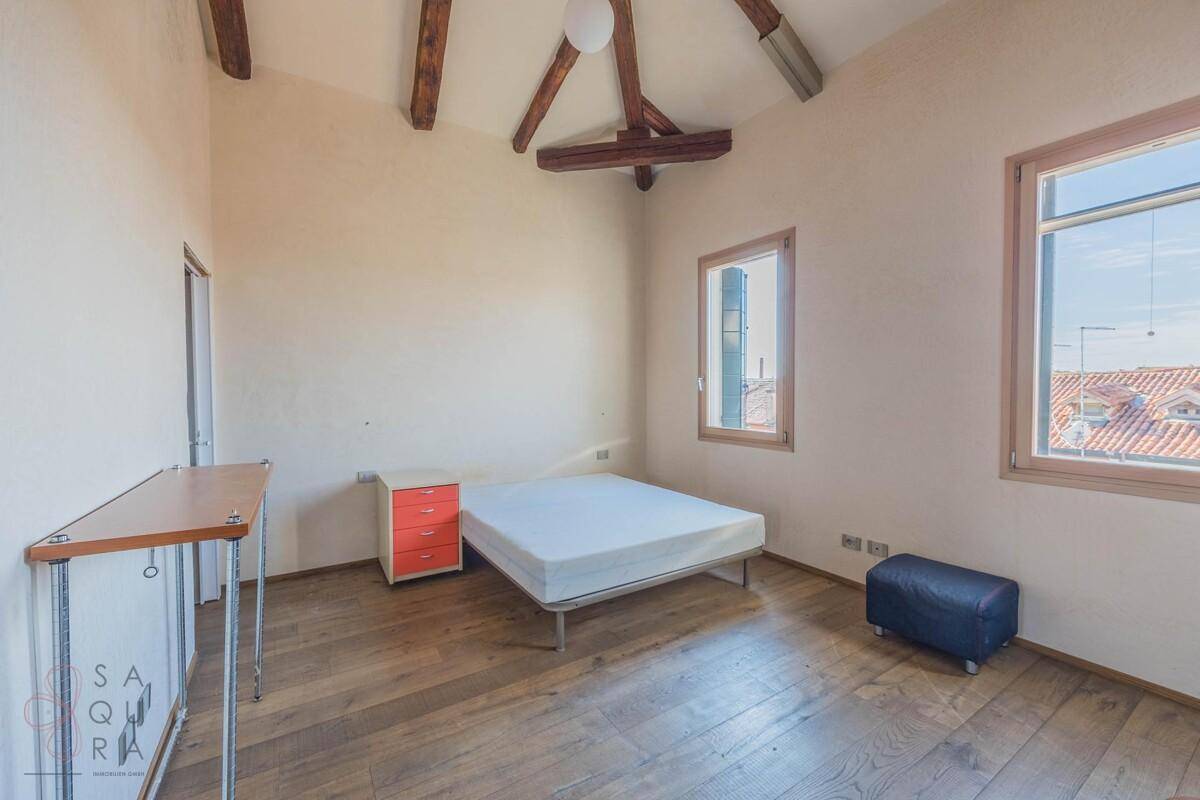 Schlafzimmer mit Doppelbett, Holzboden und sichtbaren Holzbalken, die dem Raum Charakter verleihen.