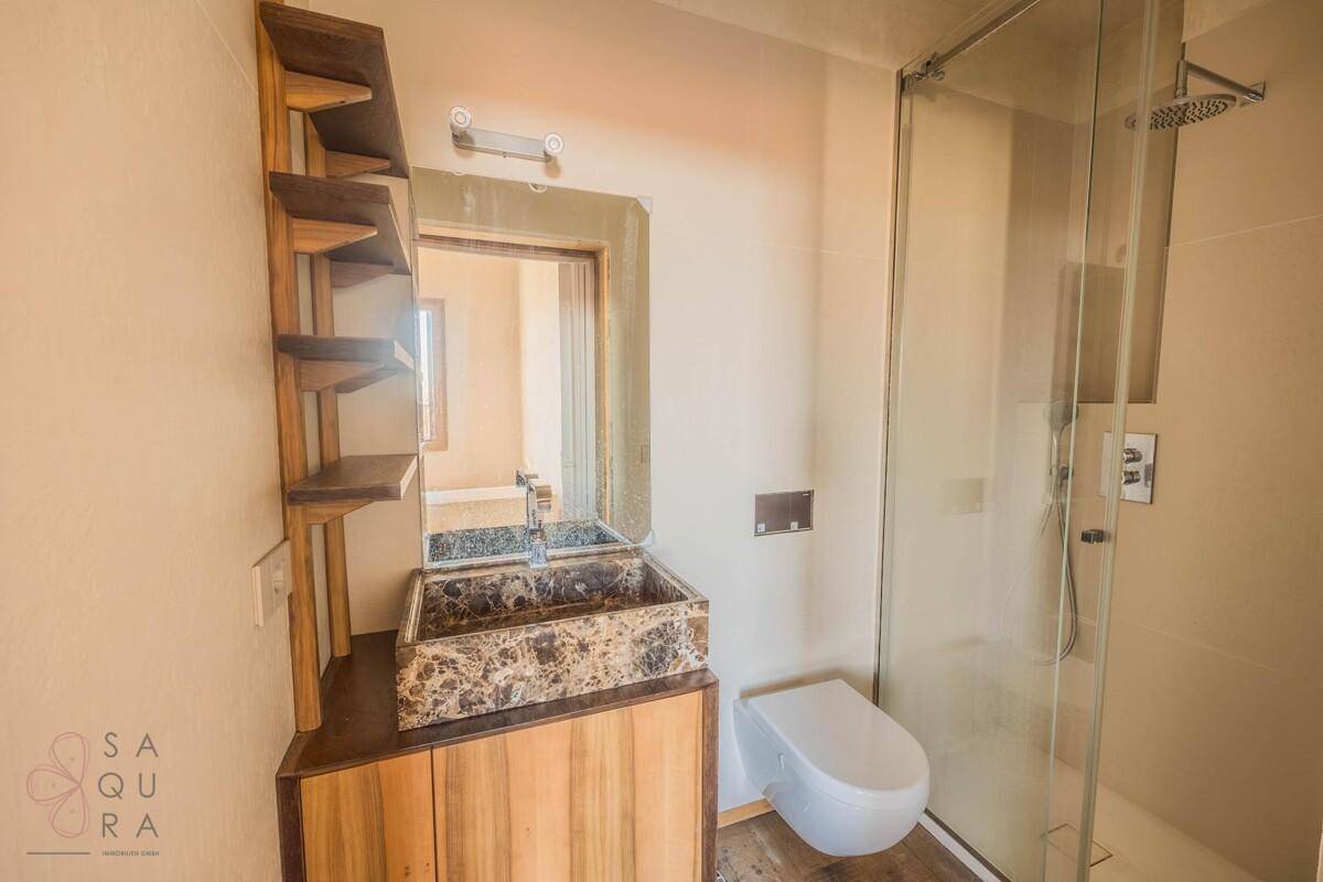 Modernes Badezimmer mit einzigartigem Steinwaschbecken, Holzunterschrank, wandhängendem WC und begehbarer Dusche.