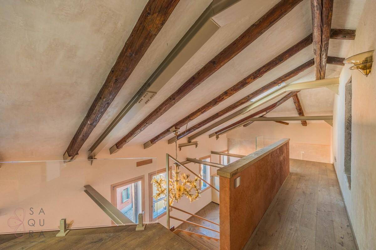 Dachgeschoss mit rustikalen Holzbalken, Holzgeländer und Blick auf die Treppe zum unteren Wohnbereich.