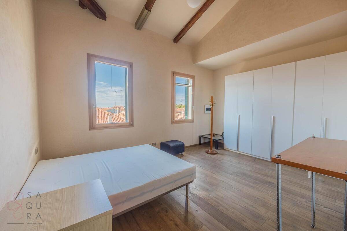 Helles Schlafzimmer mit Holzboden, Doppelbett und weißem Kleiderschrank, ergänzt durch sichtbare Holzbalken.