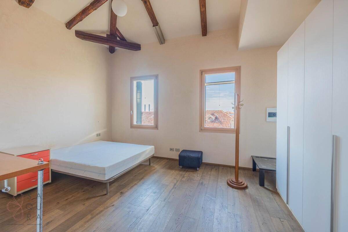 Schlafzimmer mit Doppelbett, Holzboden, weißem Kleiderschrank und sichtbaren Holzbalken unter der Decke.