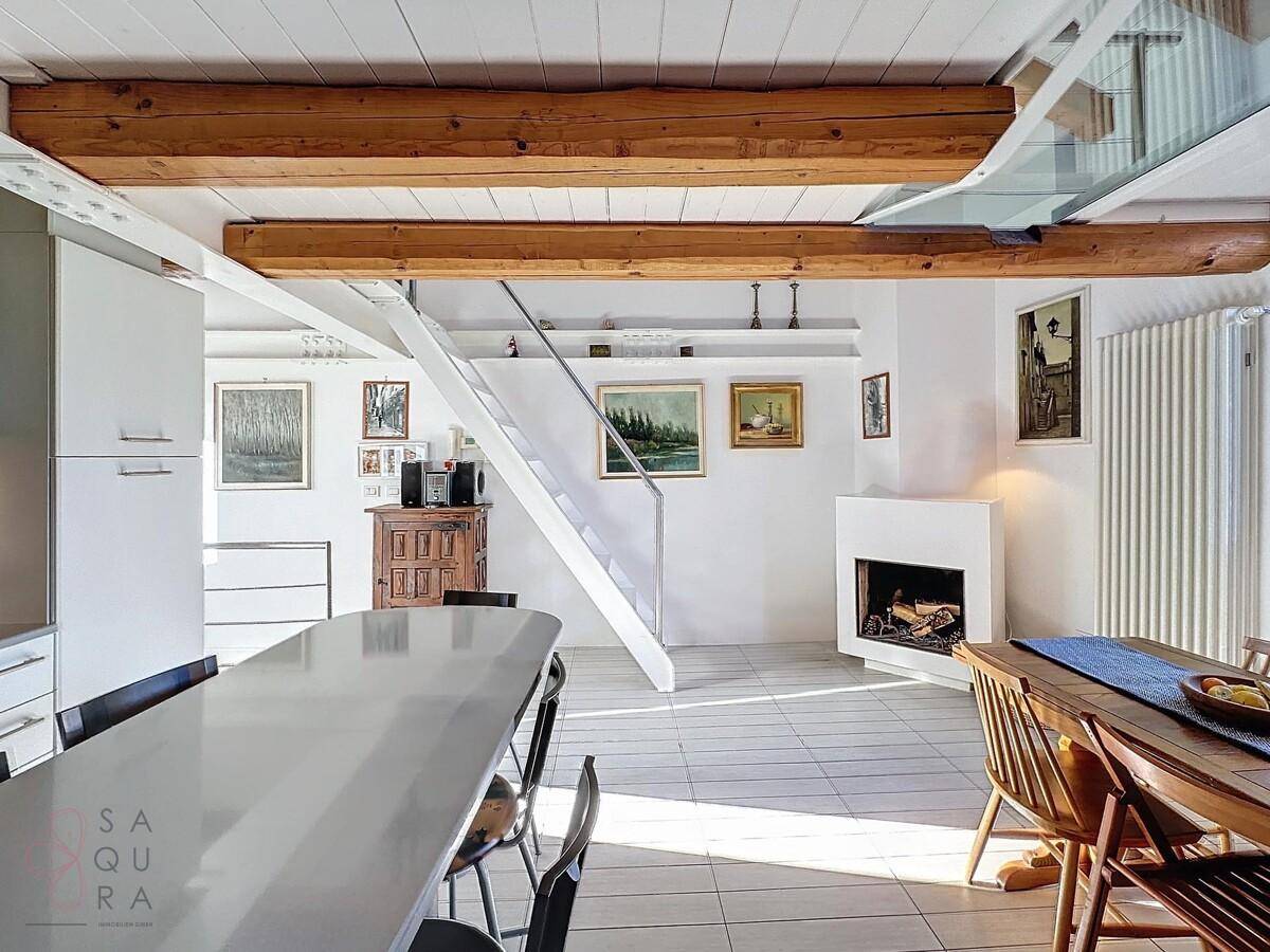 Geräumiger Wohnbereich mit Kamin, Esstisch und offener Treppe zu einer oberen Ebene.