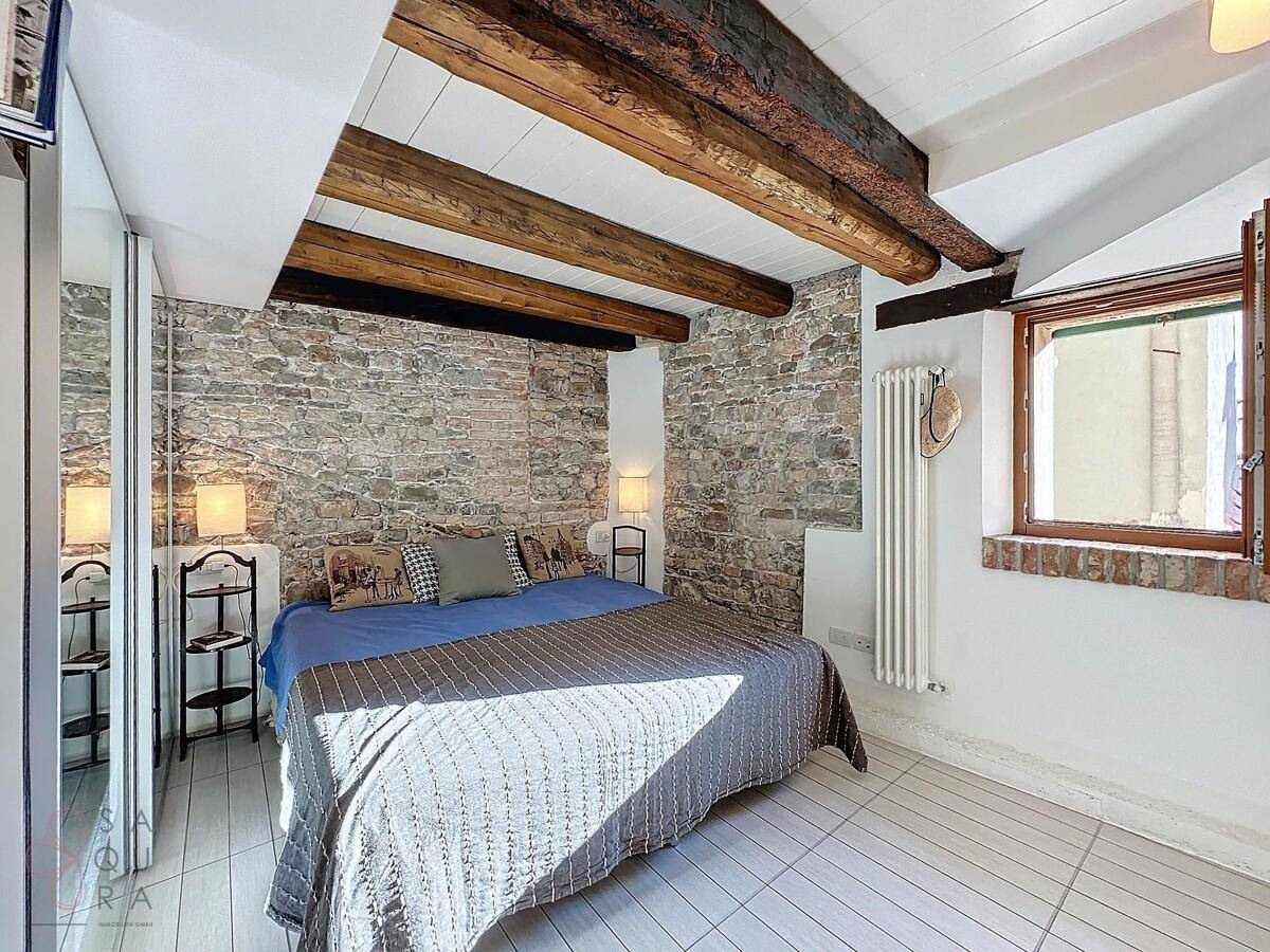 Schlafzimmer mit rustikaler Ziegelwand, Holzbalken und hellem Fliesenboden.