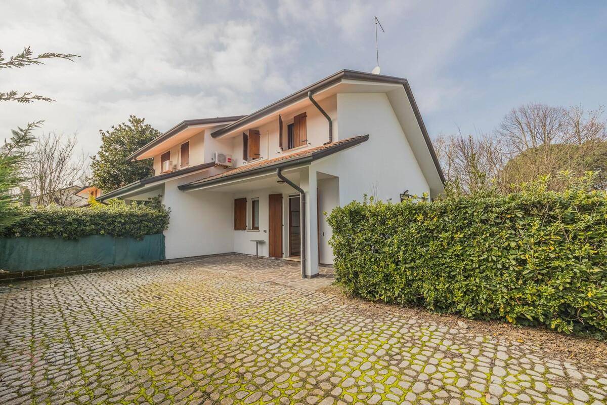 Seitenansicht des Hauses mit gepflasterter Auffahrt und üppiger Heckenbepflanzung.