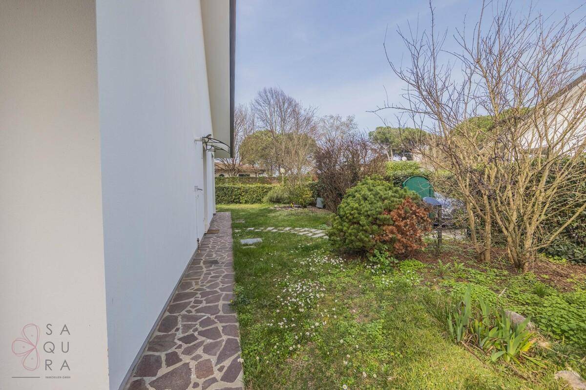 Seitenansicht des Hauses mit einem schmalen Steinweg und einem grünen Gartenbereich.