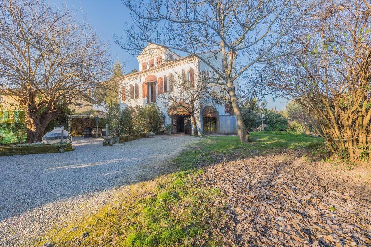 Charmantes historisches Gebäude mit weitläufigem Garten und Kiesauffahrt unter blauem Himmel.
